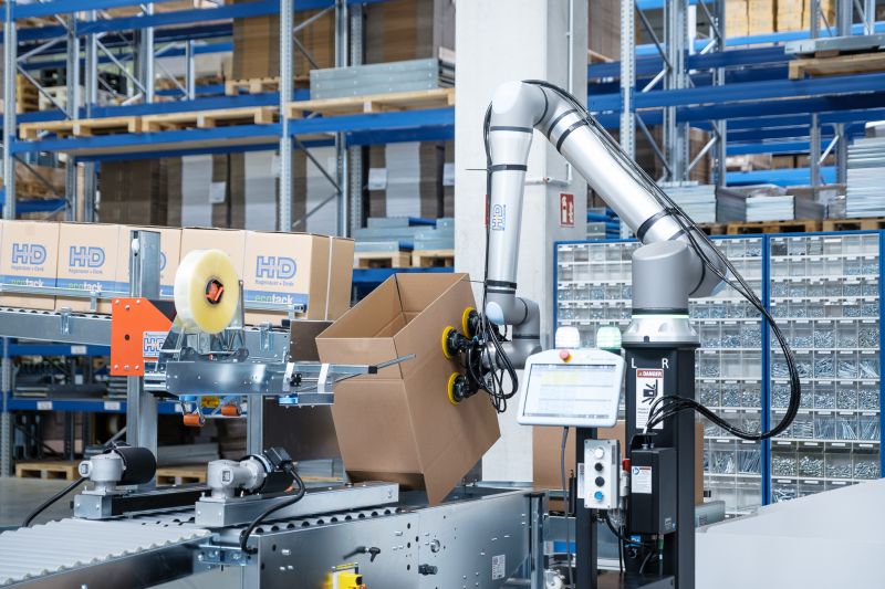 Cobot fixiert Karton in Bodenklappenfalter